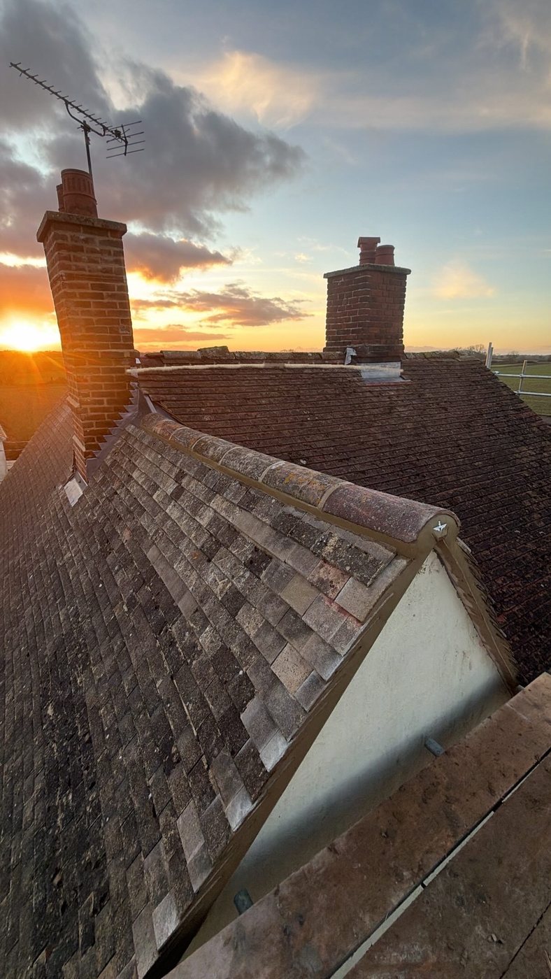 Clay-tile roof with chimneys, ridge pointing and leadwork at sunset